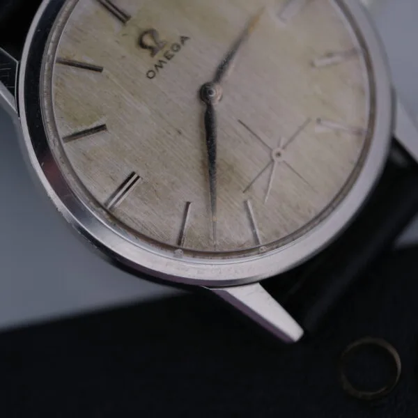An Omega Manual Wind Cal. 268 wristwatch boasts a weathered dial with Roman numeral hour markers, complemented by a leather strap and metal case. The iconic Omega logo at 12 oclock highlights its timeless elegance and classic craftsmanship.