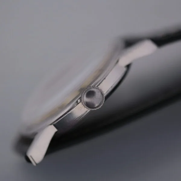 A close-up of the Omega Manual Wind Cal. 268 watch case, focused on the crown and showcasing its silver metallic finish with a partial view of the black leather strap, highlights the side profile and fine details of this elegant timepiece.