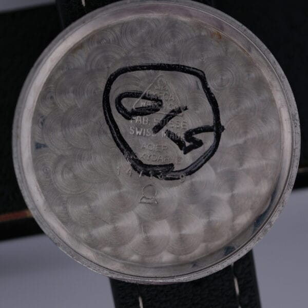 The Omega Manual Wind Cal. 268 watch case back features an engraving of the iconic logo with FAB. SUISSE, SWISS MADE, and ACIER INOXYDABLE, set against a decorative circular pattern, highlighting Omegas renowned craftsmanship.