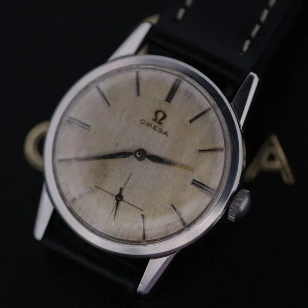 The Omega Manual Wind Cal. 268 features a cream face with bold black hour markers and two sleek hands. It has a black leather strap, elegantly displayed on a dark surface.
