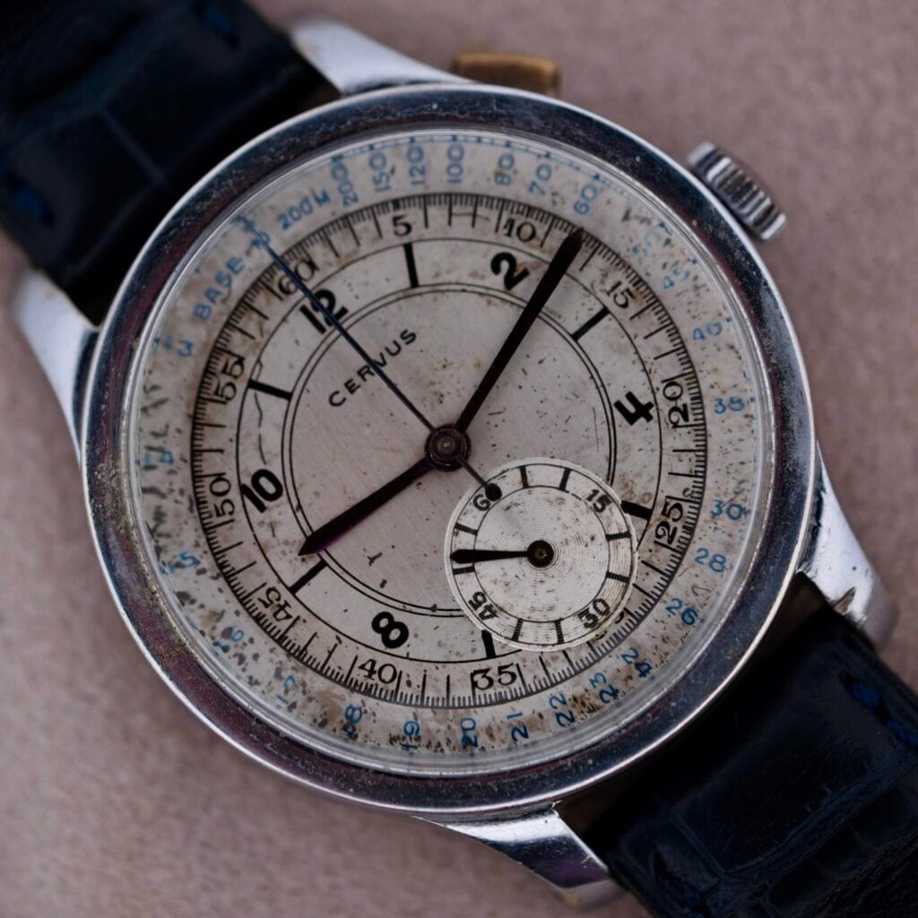 Close-up of a vintage Cevrus Monopusher Chronograph Sector Dial wristwatch, featuring a white dial, dark leather strap, visible wear, tachymeter scale, and subdial for seconds. The brand name Cervus is prominently displayed on the face.