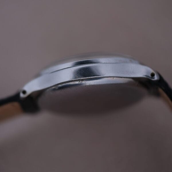 Side view of the silver Cevrus Monopusher Chronograph Sector Dial watch highlights its metallic edge and slightly domed glass. The band is visible on both sides against a blurred neutral background.