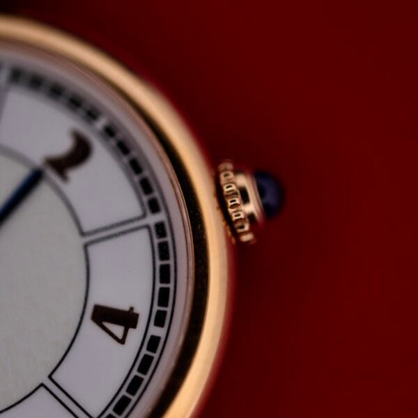 DSCF1858 Close-up of a Cartier Vendome Reference 1861 Vermeil 30mm vintage wristwatch face. It features gold edges and a crown, with black numerals at 2 and 4 on a white dial, standing out against the solid red background.