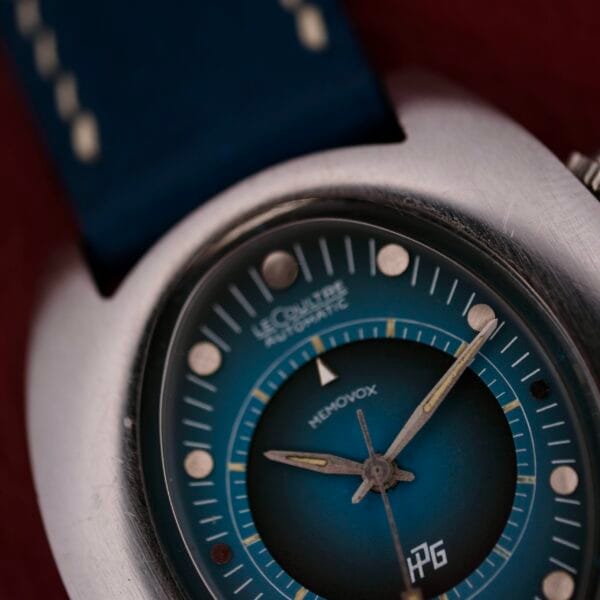 The close-up features a 1971 Jaeger LeCoultre Memovox Egg wristwatch with a striking blue gradient dial and silver casing, elegantly displaying LeCoultre Automatic and Memovox. Silver hour markers and hands complement the design, while a matching blue strap completes the look.