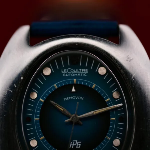 Close-up of a 1971 Jaeger LeCoultre Memovox Egg automatic watch face. The enchanting blue dial features silver and white markings with an inner alarm dial, complemented by silver-toned hands. The case exudes character with its signs of wear.
