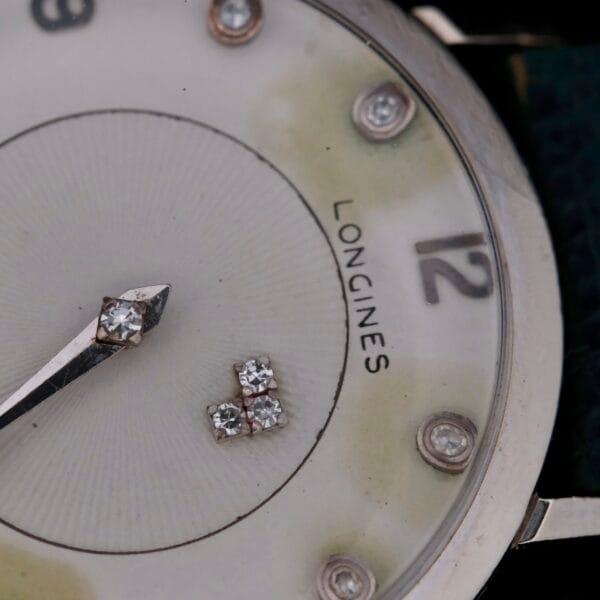 Close-up of a 1958 Longines Mystery Dial watch face in 14k white gold and diamonds, featuring diamond hour markers and a slim silver minute hand at the 10-minute mark. The face shows minor discoloration and wear, with the iconic LONGINES brand name visible on the right side.