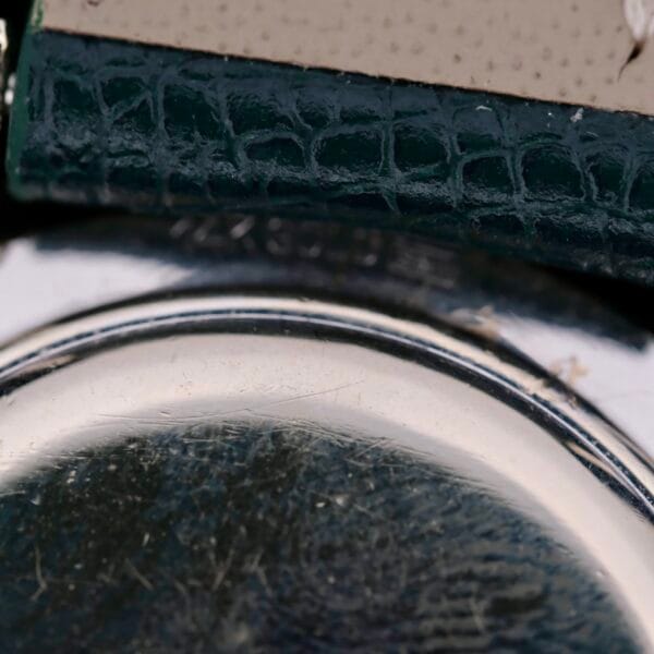 Close-up of a textured dark green leather and reflective metallic surface, likely part of a 1958 Longines Mystery Dial watch in 14k white gold with diamonds, showcasing intricate textures and slight metal wear.