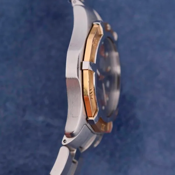 The side profile of the Tag Heuer 2000 Exclusive, with its 18k gold bezel, is set against a textured dark blue background. Its sleek design symbolizes timeless sophistication.