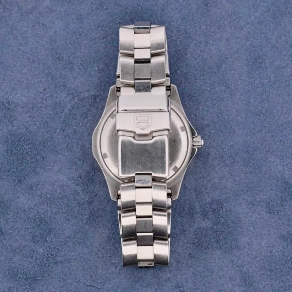 A Tag Heuer 2000 Exclusive wristwatch with an 18k gold bezel and metal link bracelet is displayed on a textured blue background, showcasing the back view of its clasp and case.