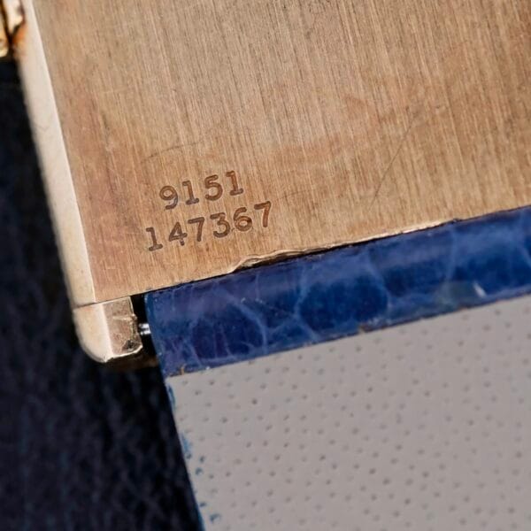 A close-up reveals a metallic surface with the precise engravings 9151 and 147367, reminiscent of the precision found in a Piaget Tank Ref 9151 18k Gold Manual Wind. Below, a blend of blue and gray textures adds depth to the enigmatic design.