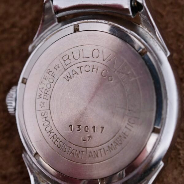 Close-up of a vintage 1956 Bulova Manual Wind Calibre 11AC Waffle Dial watch back, engraved with Waterproof, Watch Co, Shock Resistant, and Anti-Magnetic. The serial number 13017 and L7 showcase the classic craftsmanship of this timeless piece.