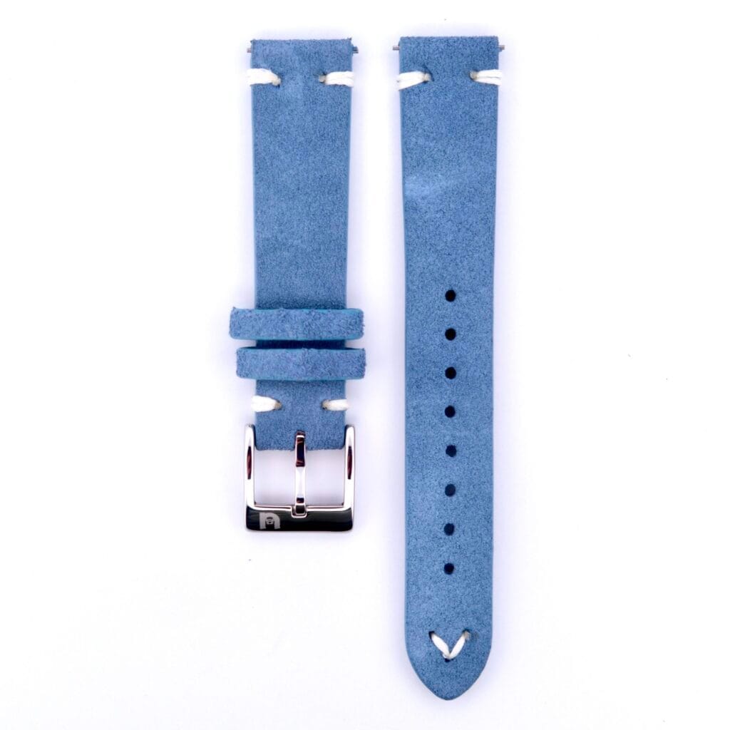 The Powder Blue Suede Watch Strap Vintage Stitch is shown against a white background. It features two parts: one with a silver buckle and another with multiple adjustment holes. White stitching decorates both ends, enhancing its timeless appeal.