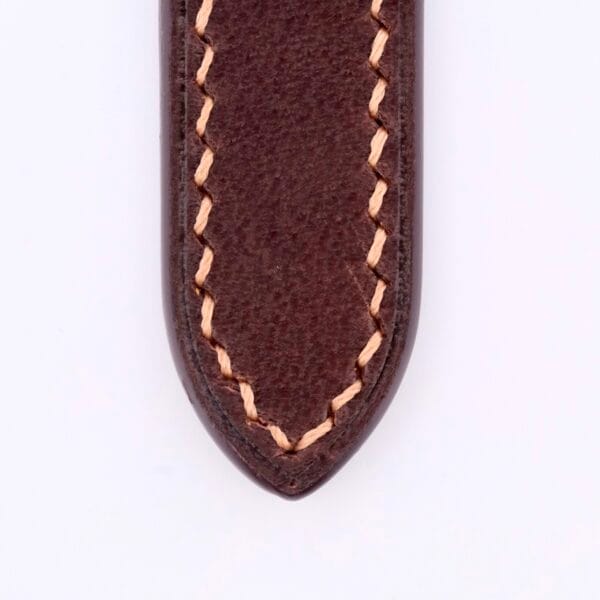 The Dark Brown Genuine Horween Shell Cordovan Watch Strap showcases a close-up of its leather with beige zigzag stitching featuring smooth texture, an elegantly tapered design, and a pointed tip that highlights exquisite craftsmanship.