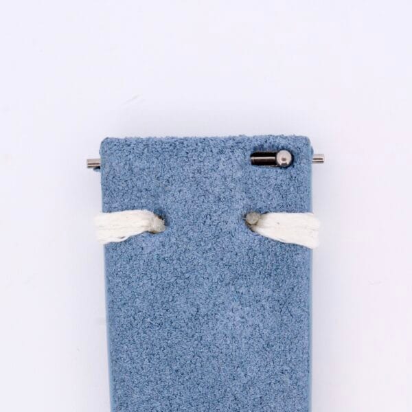 A close-up of the Powder Blue Suede Watch Strap Vintage Stitch showcases a metal pin at the top and two white threads looped through, reminiscent of a vintage watch strap, set against a plain white background.
