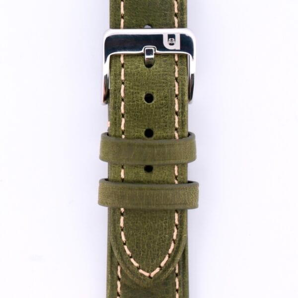 A close-up of the Simple Stitch Vintage Leather Watch Strap Matte Finish reveals its green leather with beige stitching. The silver buckle is centered above two loops, highlighting the natural grain and texture of the leather.