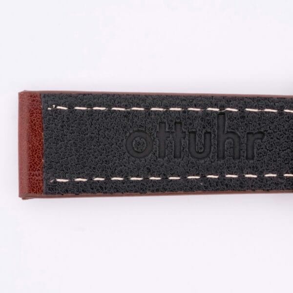 Close-up of the Simple Stitch Classic Leather Watch Strap with ottuhr embossed on it. The strap is black with white stitching and a brown edge, exuding timeless elegance.