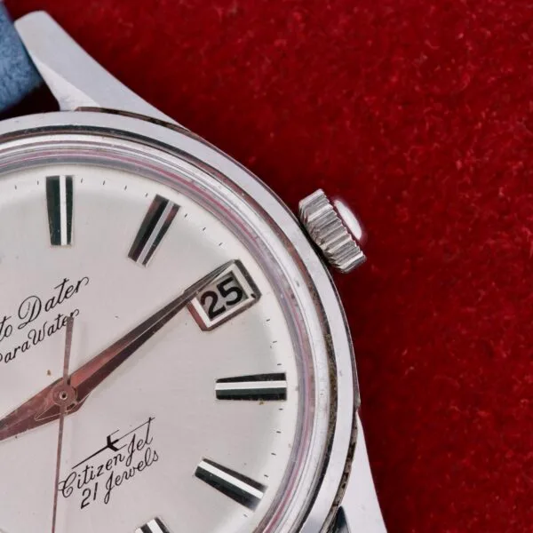 A close-up of the Citizen Jet Auto Dater Automatic Para Water wristwatch on a textured red surface reveals silver hour markers, a date window set to the 25th, and black lettering stating Parawater and 21 jewels on the face.