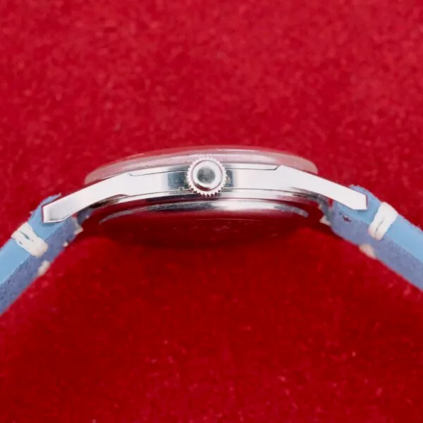Side view of a Citizen Jet Auto Dater Automatic Para Water watch with a blue leather strap on a red textured background. The silver case features a visible crown on the right side, highlighting timeless elegance and precision.