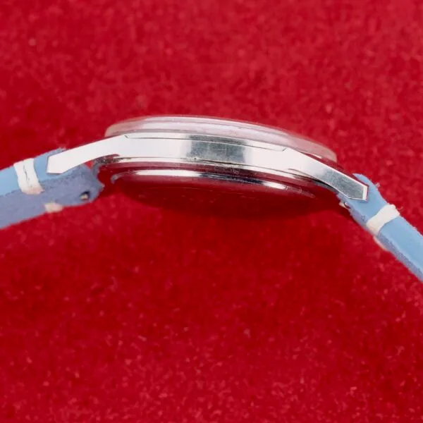 A side view highlights the elegance of a Citizen Jet Auto Dater Automatic Para Water watch, featuring a sleek silver case and light blue leather strap, beautifully contrasted against a vibrant red background.