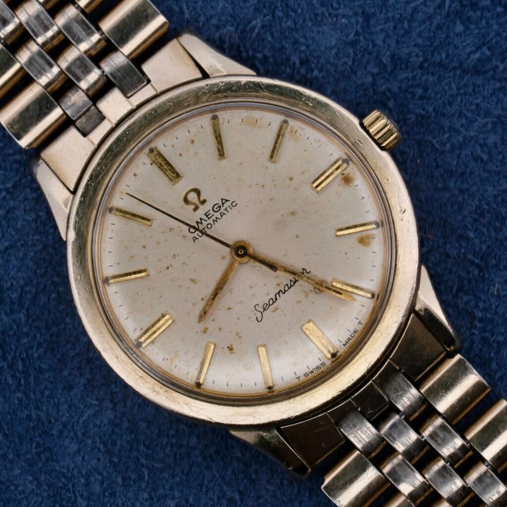 A vintage Omega Seamaster Automatic Cal. 550 with a gold bracelet features a round, gold-toned case and a slightly weathered white dial. It has gold hour markers and hands with Omega Seamaster Automatic elegantly scripted below the 12 oclock position.