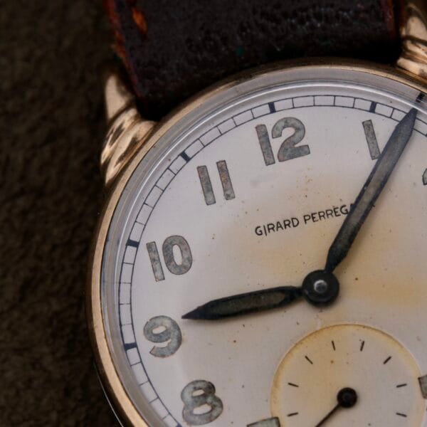 Close-up of the Girard Perregaux Military Dial Small Seconds wristwatch, featuring a white dial with black numerals and hands. The design includes a small seconds subdial at 6 oclock, and Girard Perregaux is prominently displayed below the 12 oclock mark.