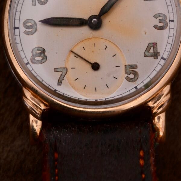 A close-up view of the Girard Perregaux Military Dial Small Seconds wristwatch showcases its vintage charm, with a white dial, black numerals, dark hands, and a small seconds subdial. This piece features a gold-toned case paired with a brown leather strap.