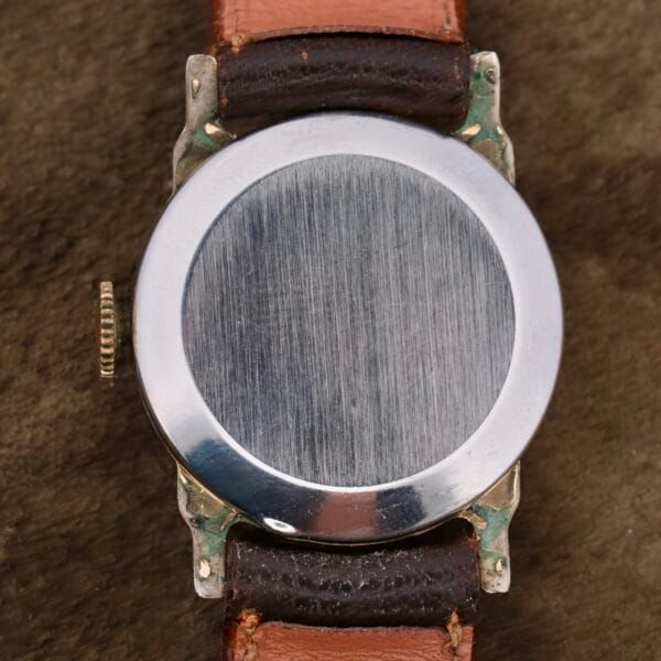 The Girard Perregaux Military Dial Small Seconds watch, featuring a blank metal face without markings or hands, is attached to a worn brown leather strap evoking military style and displayed on a textured dark brown surface.