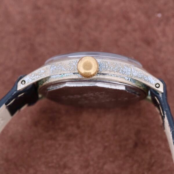 Close-up of a vintage WWII Military ELGIN General Service Watch ORD. DEPT. U.S.A. 1944, highlighting the worn textured metal case and gold-toned crown with a black leather strap showing wear against a rich brown background.