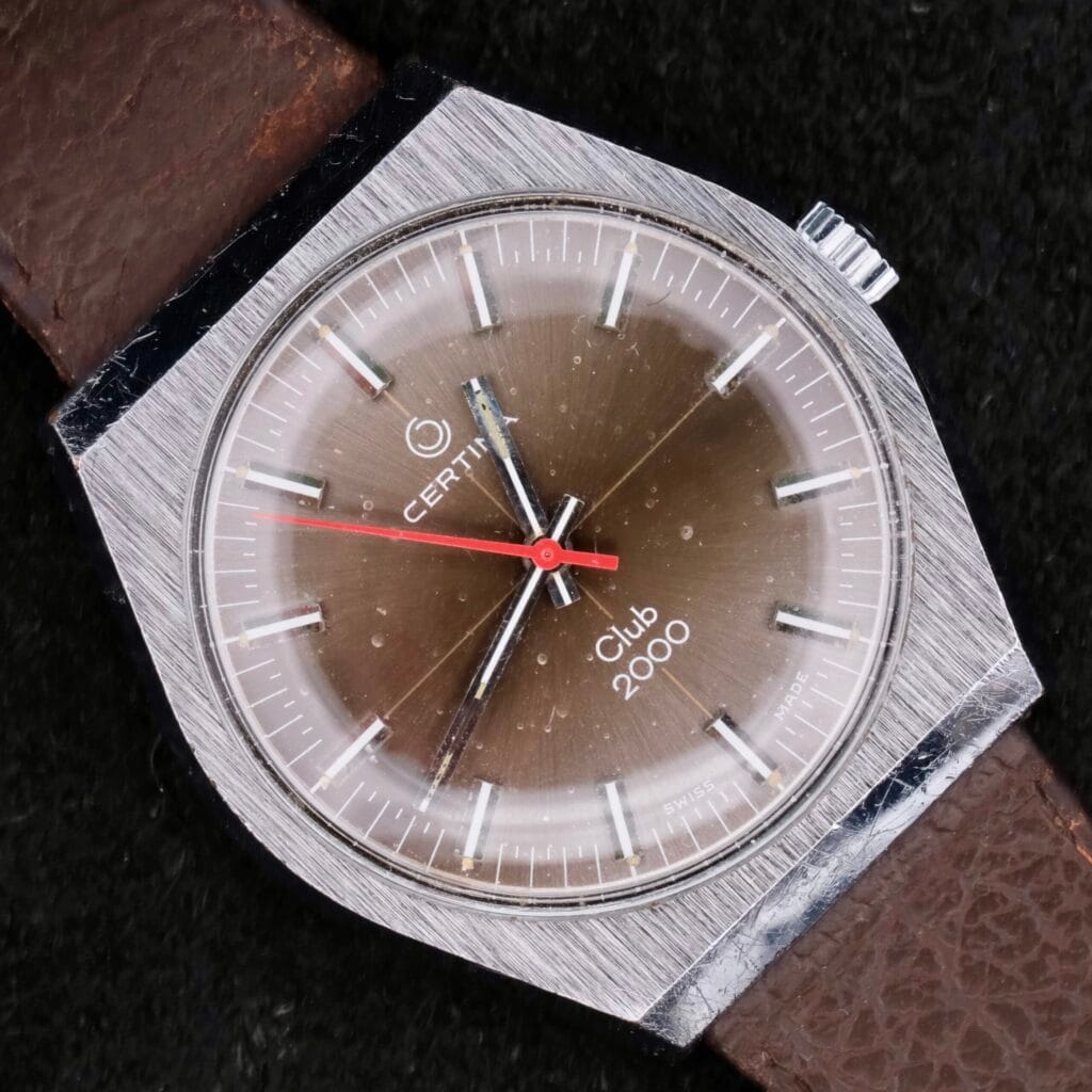 A Certina Club 2000 Cal. 2502 wristwatch from the 1970s, featuring a brown dial, silver case, and a brown leather strap.
