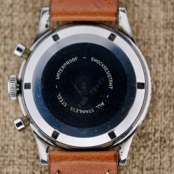 The back of a Nivada Grenchen Aviator Sea Diver Chronograph 1st Gen with a brown leather strap, featuring engraved text WATERPROOF, SHOCKRESISTANT, ALL STAINLESS STEEL on its black circular backplate.
