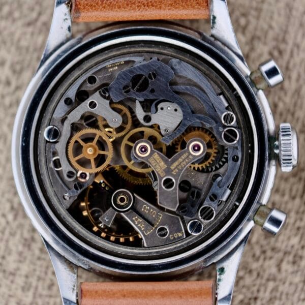 A detailed view of the Nivada Grenchen Aviator Sea Diver Chronograph 1st Gen showcases its intricate movement and gears through an open back casing. This classic piece features a silver frame and a brown leather strap, highlighting its elegant craftsmanship.