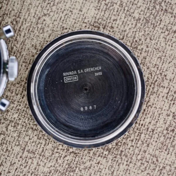 A close-up of the inside case back of a Nivada Grenchen Aviator Sea Diver Chronograph 1st Gen, showing engraved text and the number 8987, on a textured beige surface.