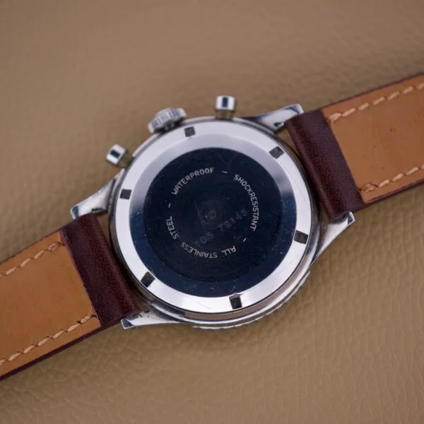 Back of a Nivada Grenchen Aviator Sea Diver Chronograph 1st Gen wristwatch with a brown leather strap, displayed on a tan textured surface.