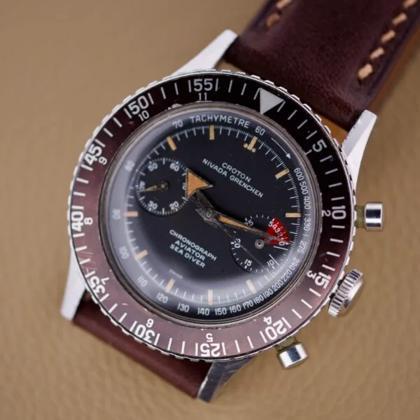 Nivada Grenchen Aviator Sea Diver Chronograph 1st Gen wristwatch with a brown leather strap, displayed on a tan surface.