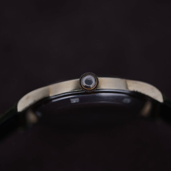 Close-up side view of an Omega Seamaster Gold Automatic 354 against a dark background, focusing on the metallic-finished crown. The elegant design is highlighted by a portion of the dark strap visible in the image.