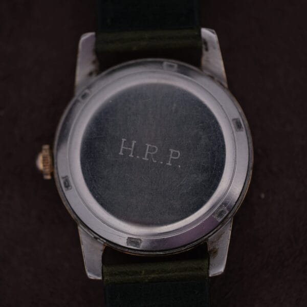 A close-up of the back of an Omega Seamaster Gold Automatic 354 wristwatch with H.R.P. engraved on the metal. The watchs dark strap enhances its allure against a shadowy background.