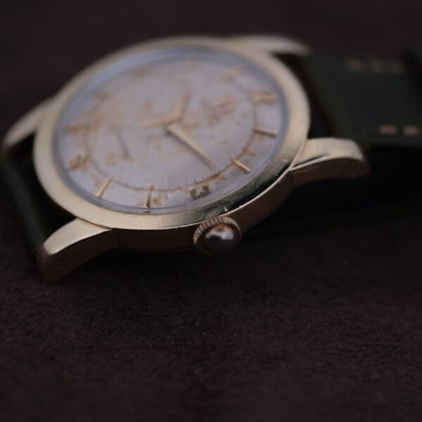 Close-up of the Omega Seamaster Gold Automatic 354, featuring a round tarnished face and gold-tone casing. Set against a dark background, it showcases its black leather strap and simple hour markers.