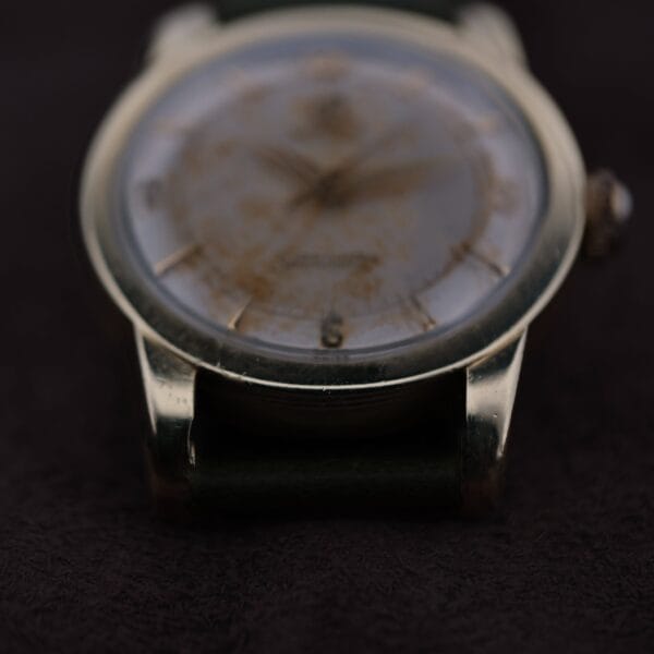 Close-up of a vintage Omega Seamaster Gold Automatic 354 with a blurred, worn face and metallic case resting on a dark surface, its details obscured, suggesting age and use.