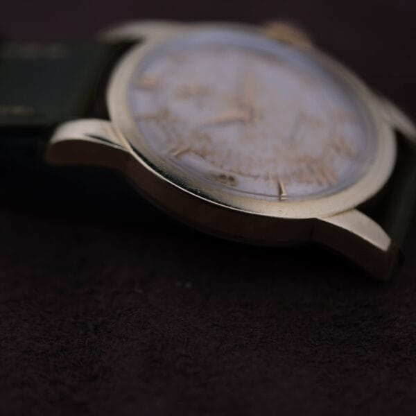 Close-up of the Omega Seamaster Gold Automatic 354 wristwatch with a blurred dial and dark background, highlighting the watchs polished edge and exquisite details.