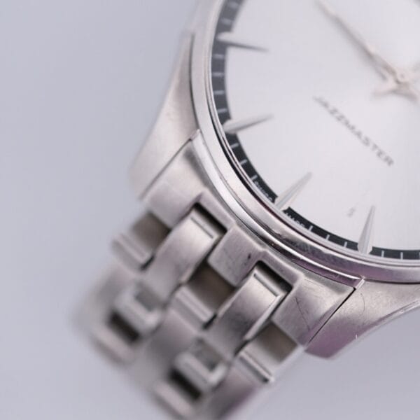 A close-up of the Hamilton Jazz Master Stainless Steel wristwatch highlights its metal link band and partially visible minimalist face, elegantly inscribed with JAZZMASTER and featuring fine markers and hands.