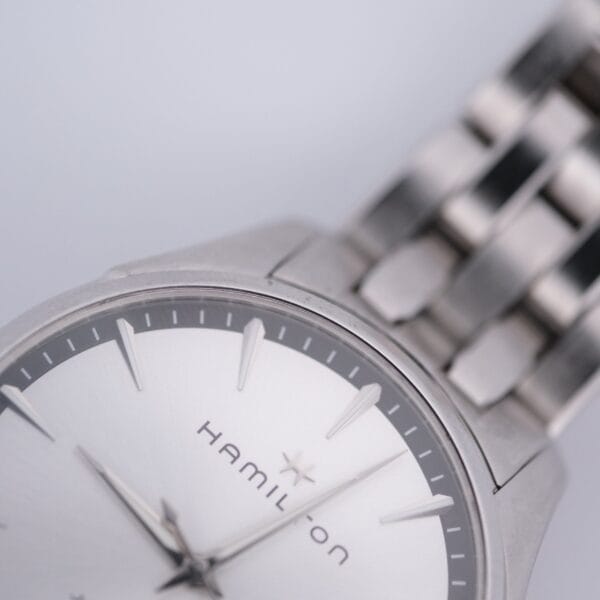Close-up of the Hamilton Jazz Master Stainless Steel watch, with a silver band and sleek dial. It features sharp hour markers and slender hands on a light background.