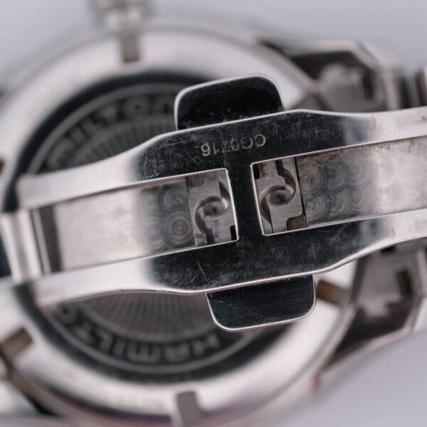 Close-up of a stainless steel watch clasp with engraved text, showcasing intricate design details reminiscent of the Hamilton Jazz Master.