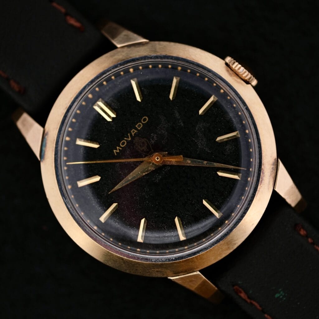 A vintage Movado Ref. 18240 Francois Borgel Gold Top wristwatch for the Hong Kong market featuring a black leather strap and black face with gold hour markers.