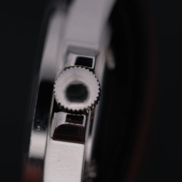 Close-up of the metallic crown on the sleek Swiss Army Day/Date Field Watch Swiss Made. The serrated edges stand out against a dark backdrop, emphasizing its polished, reflective surface.