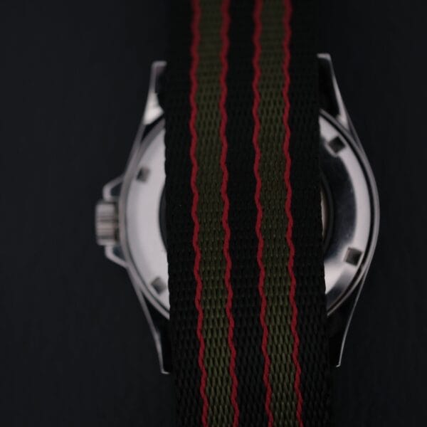 A close-up image of the Swiss Army Day/Date Field Watch Swiss Made features a nylon strap with black, green, and red stripes. The strap covers much of the watch face, while the partially visible metal casing exudes rugged sophistication typical of Swiss craftsmanship.