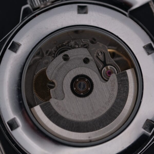 Close-up of a Swiss Army Day/Date Field Watch Swiss Mades open back, revealing intricate mechanical movement. Visible metal gears and components showcase the timepieces craftsmanship and engineering.