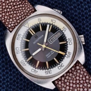 Bulova Accutron Deep Sea 666 “Devil Diver” Inner Bezel wristwatch with brown strap, black dial, and day-date display, displayed on a blue textured background.