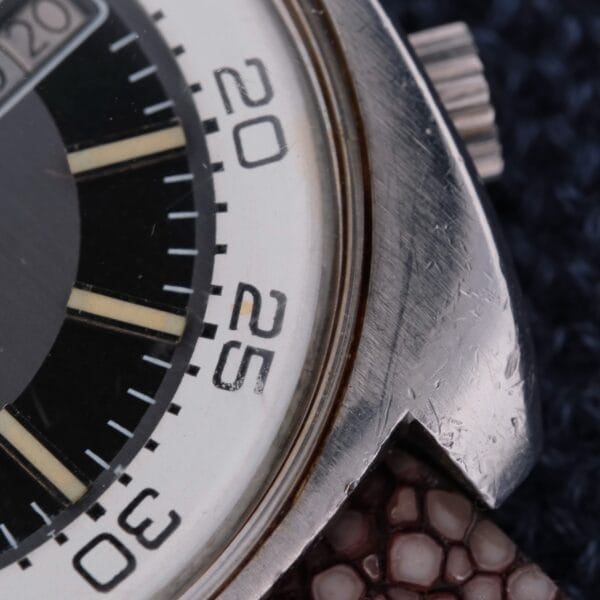 A close-up of a vintage Bulova Accutron Deep Sea 666 “Devil Diver” watch face in a silver-tone case, displaying detailed markings. The timepiece features a textured brown leather band resting elegantly on dark fabric, evoking the classic Devil Diver era.