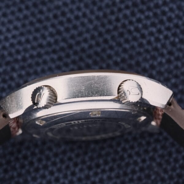 Close-up of a Bulova Accutron Deep Sea 666 “Devil Diver” Inner Bezel silver watch side, highlighting its unique design with two crowns labeled 0 and 1. Set against a textured dark blue backdrop, it exudes an elegance typical of the Devil Diver series.