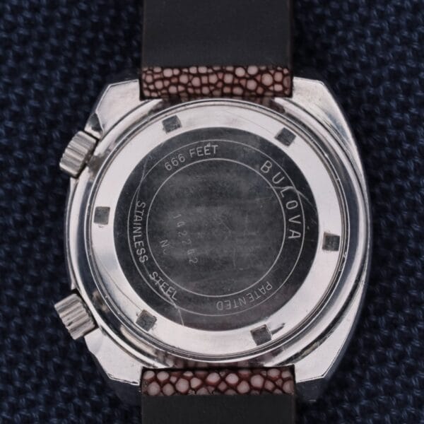 The Bulova Accutron Deep Sea 666 Devil Diver Inner Bezel watch showcases an engraved back with 666 Feet and a serial number, paired with a durable black strap featuring brown textured padding for style.